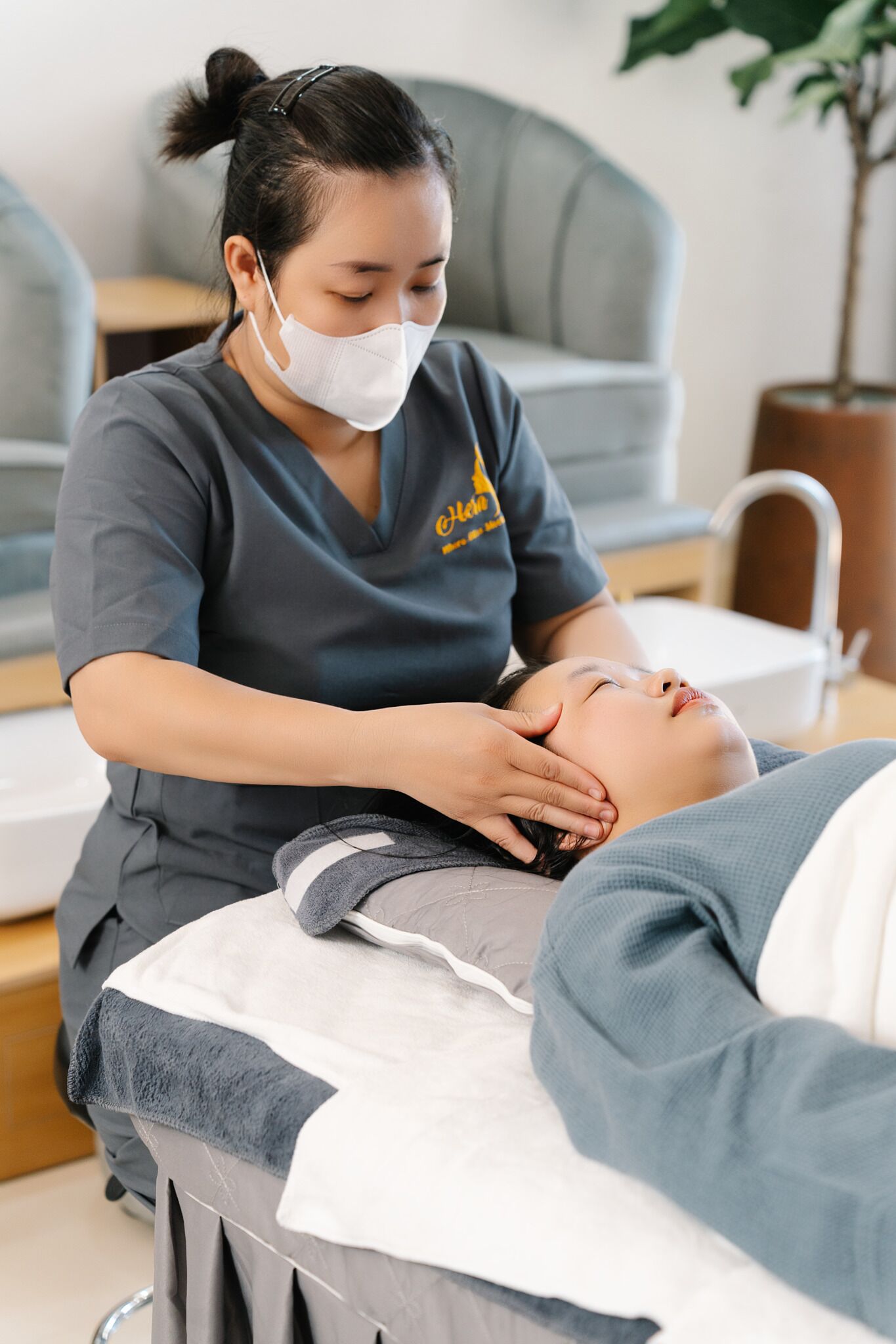 A person receiving a massage in a room with a grey sofa and a plant in the background.