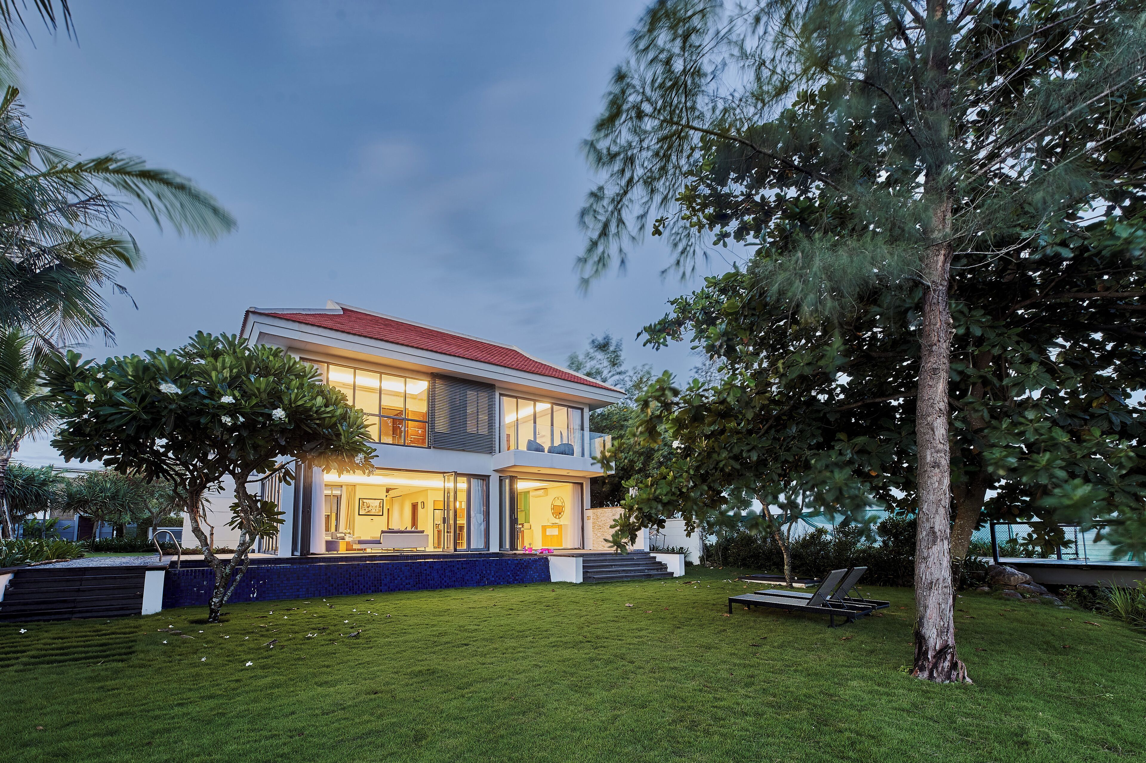 A modern two-story house with a red roof, large windows, and a well-maintained lawn.