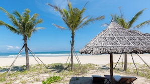 A beach with palm trees, a thatched-roof hut, and lounge chairs. - Danang Private Swimming Pool Villa (Da Nang)