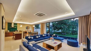 A modern living room with a sectional sofa, a coffee table, and a TV. There is a kitchen area with a dining table and chairs. - Danang Private Swimming Pool Villa (Da Nang)