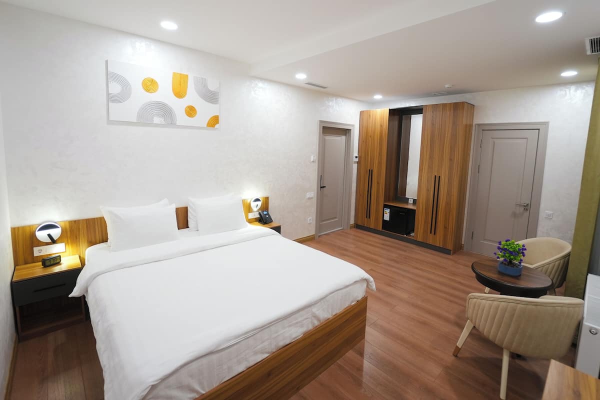 A modern hotel room with a large bed, bedside tables, a desk, a chair, and a wardrobe.