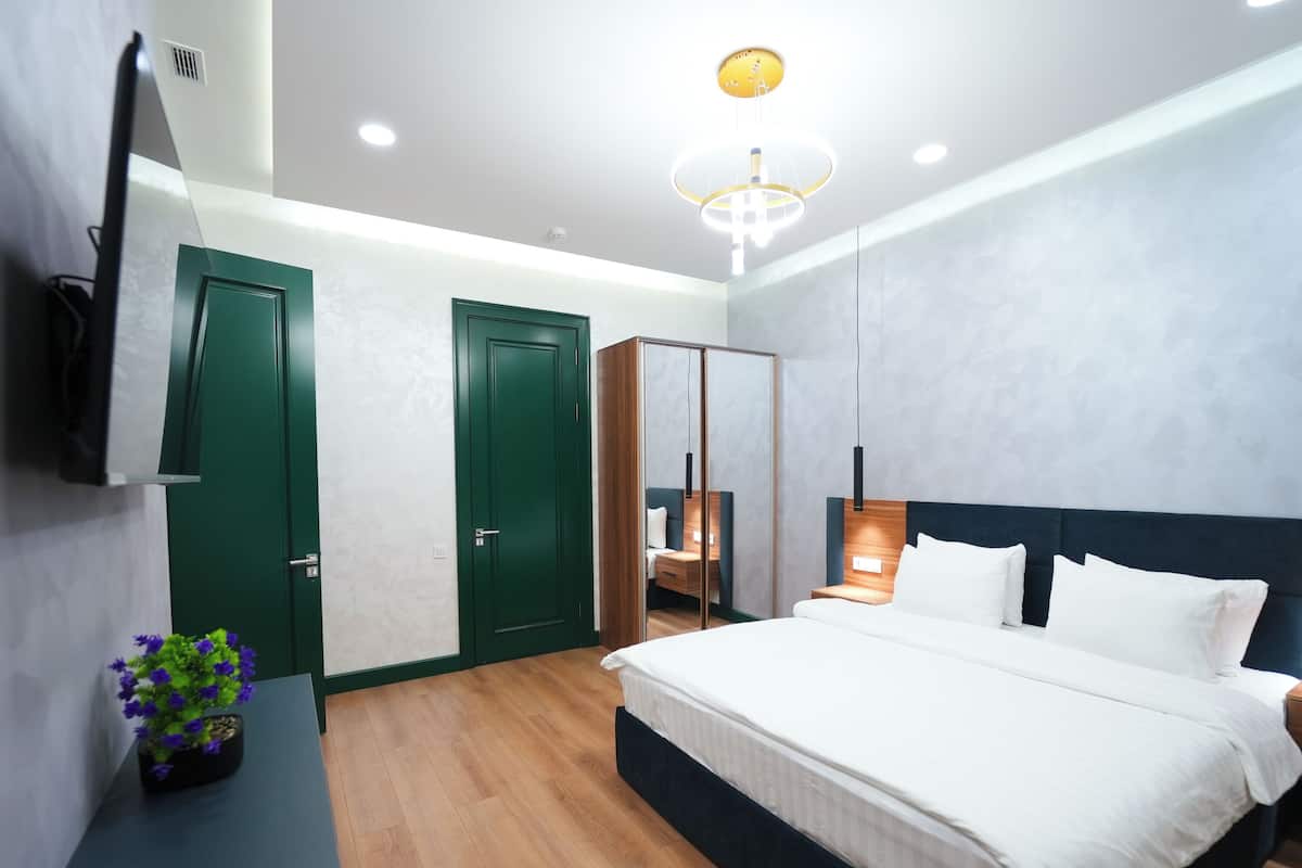 A modern bedroom with a large bed, a bedside table, a mirror, and a green door.