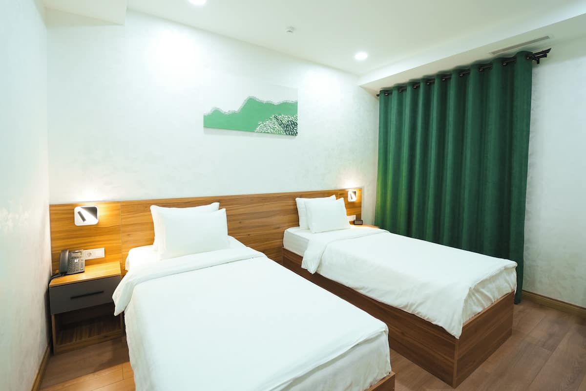 A hotel room with two single beds, a wooden headboard, a nightstand with a phone, and a green curtain.
