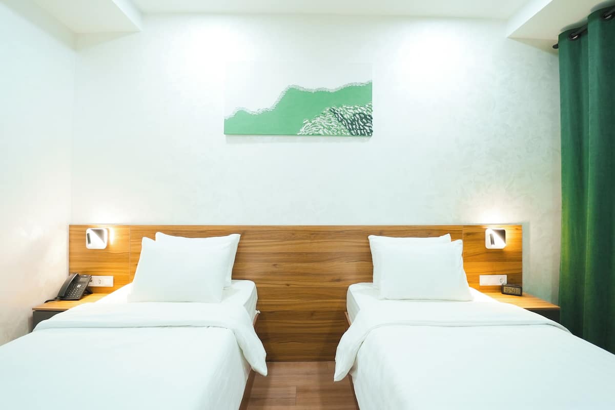 A hotel room with two beds, a wooden headboard, bedside lamps, a telephone, and a painting on the wall.
