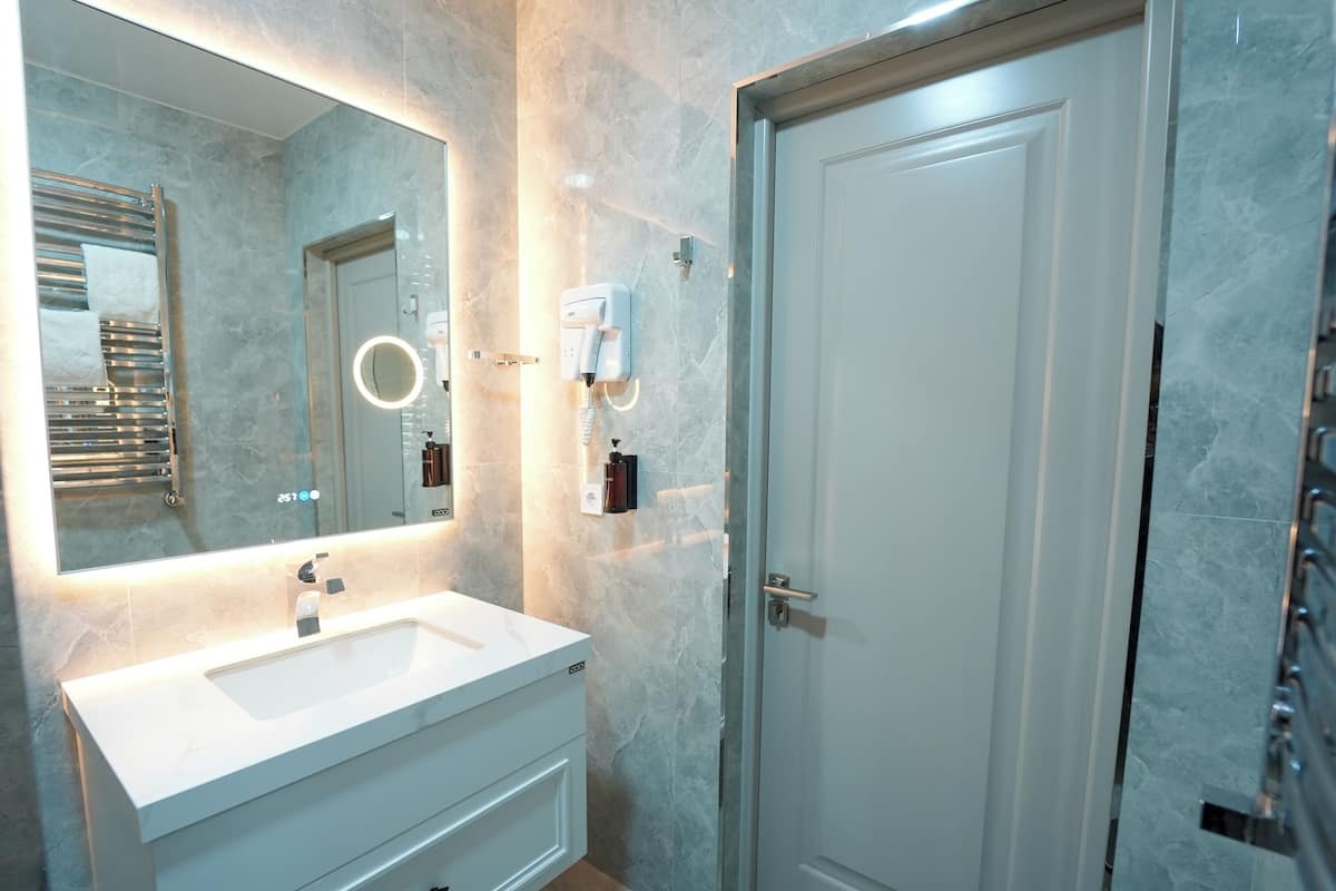 A bathroom with a white sink, a large mirror, a towel rack, a hairdryer, and a door.