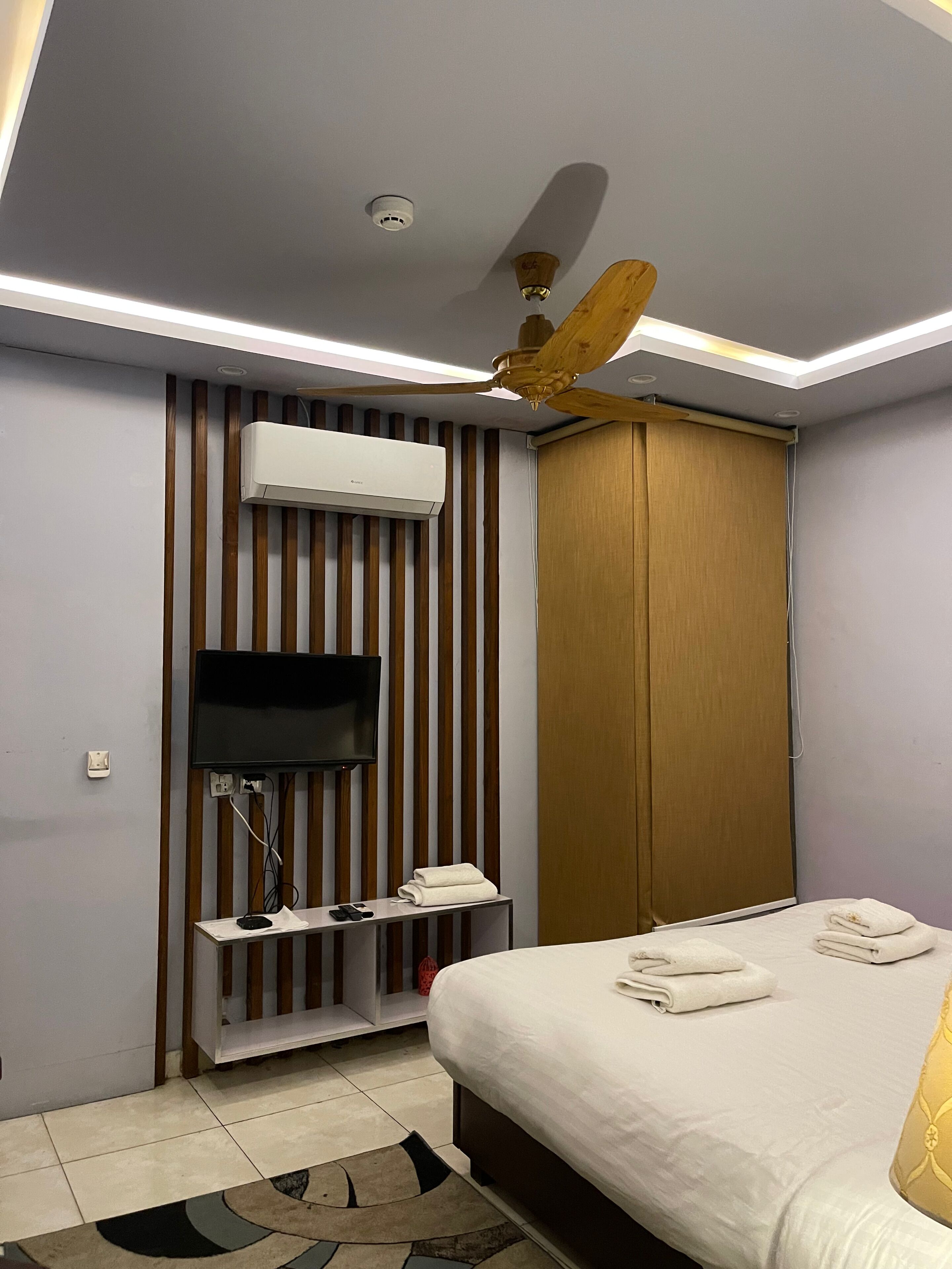 Una habitación de hotel moderna con cama, televisión de pantalla plana, aire acondicionado, ventilador de techo y armario de madera.