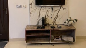 Egy modern nappali márványfalakkal, egy síkképernyős televízióval, amelyet egy fa bútor fölé szereltek, és egy piros, mintás szőnyeggel a padlón.