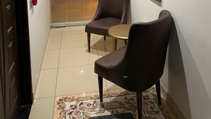 Egy szállodai folyosó, amelyen egy ülősarok, egy képkeretbe foglalt festmény és egy szobába vezető ajtó található.