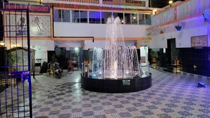 A courtyard with a central fountain, a multi-story building with balconies, and a signboard. - Hotel Nilay By GRB (Kahalgaon)