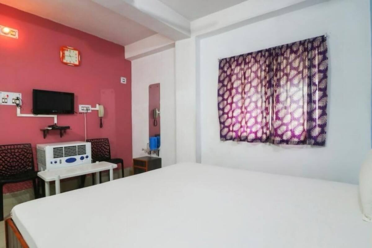 Une chambre d’hôtel équipée d’un lit, d’une télévision, d’un climatiseur, d’un bureau et d’une fenêtre avec des rideaux à motifs.