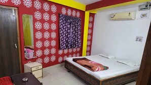 A bedroom with a bed, a small table, a chair, a wardrobe, and a wall-mounted air conditioner. - Hotel Nilay By GRB (Kahalgaon)