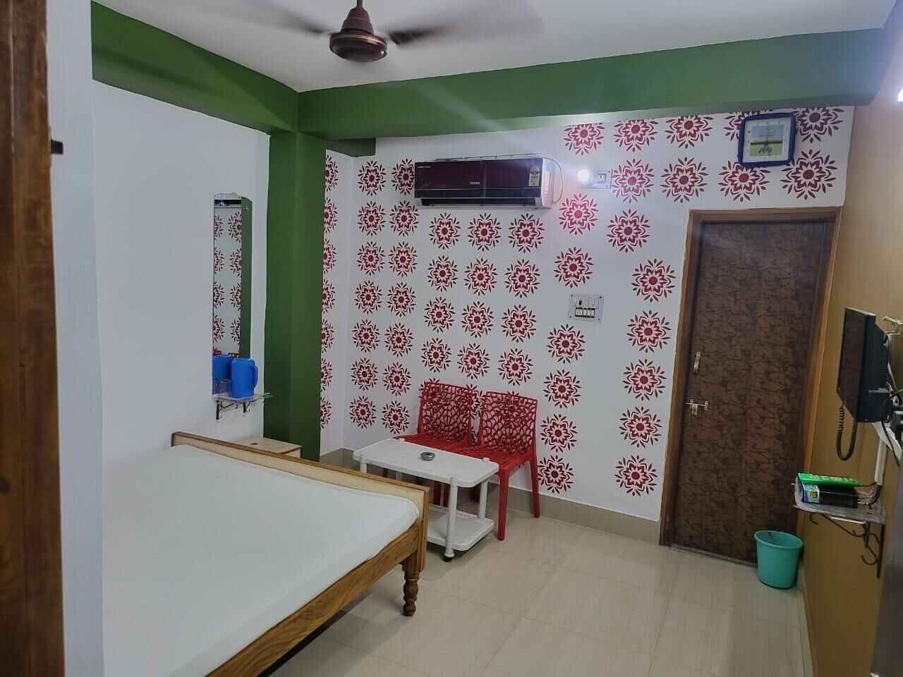 Quarto com cama, mesa e cadeira. Há um ar condicionado na parede e uma porta com tranca.