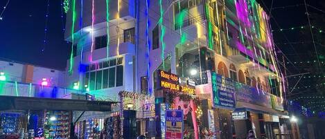 A building with a sign for 'Manjula Banquet' and a 'Hotel Mil' sign, featuring a multi-story structure with balconies and string lights.