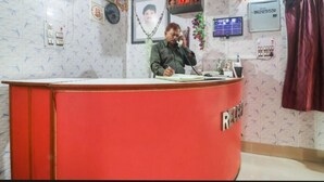 A reception desk with a red counter, framed pictures on the wall, and a clock. - Hotel Nilay By GRB (Kahalgaon)