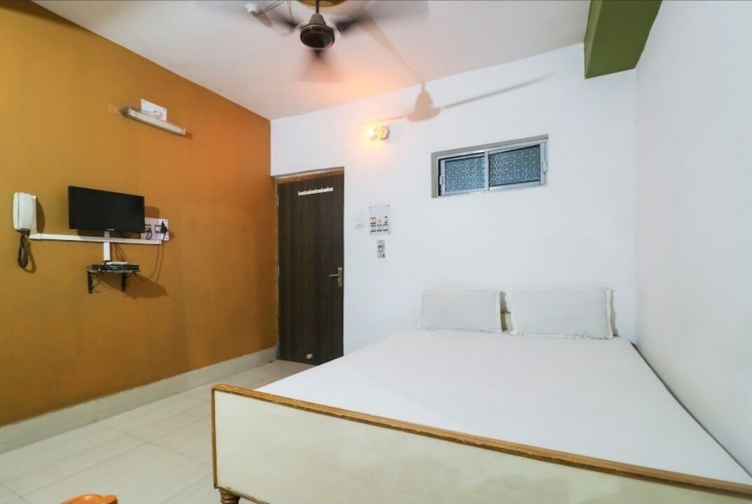A bedroom with a bed, a television on a stand, a door, and a window.