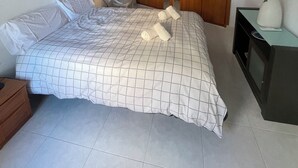 Ein Schlafzimmer mit einem großen Bett, einem Holzschrank, einem kleinen Tisch mit einer Vase und einem Bild an der Wand.