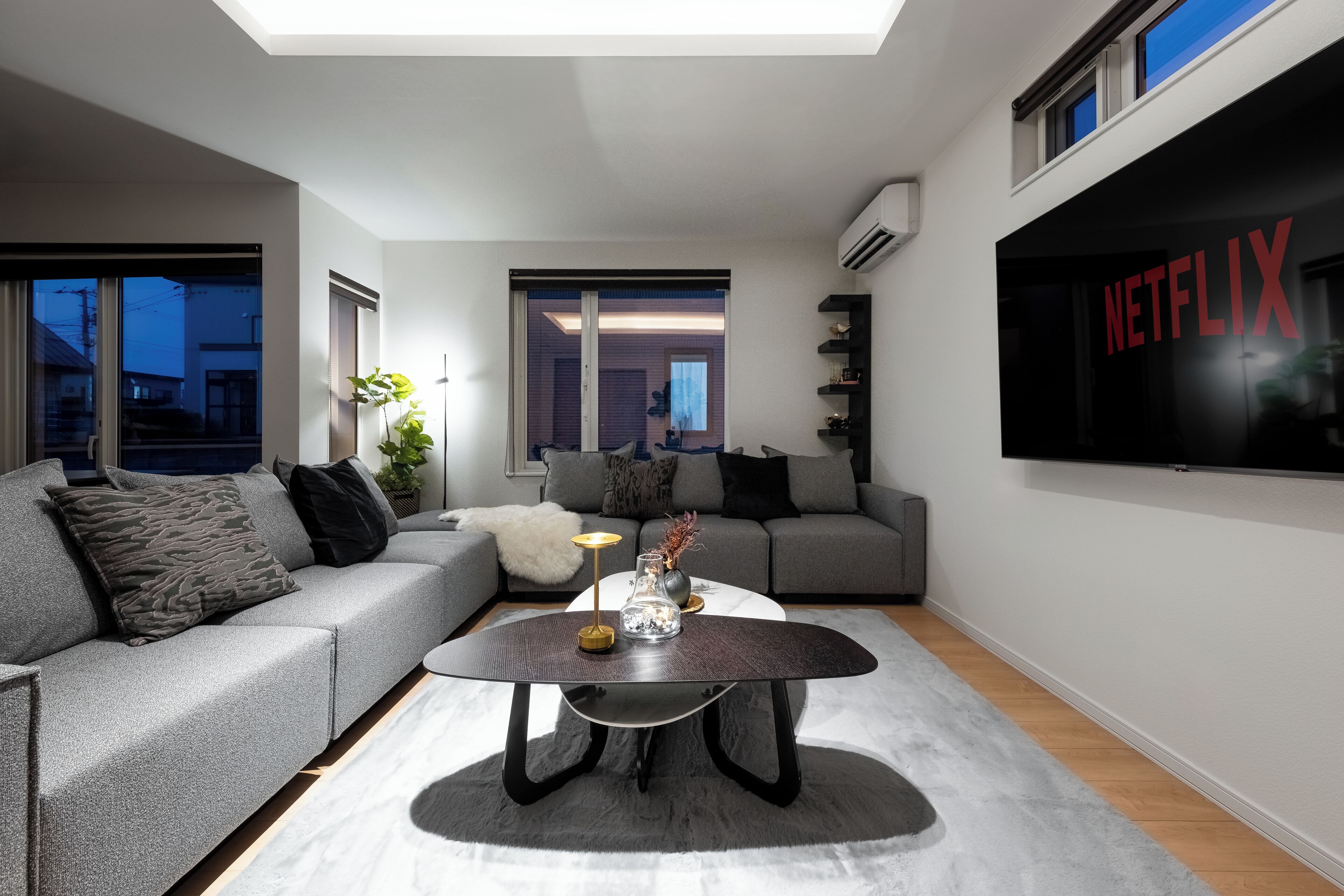 A modern living room with a grey sofa, a coffee table, and a large TV screen displaying the Netflix logo.