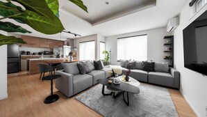 Ein modernes Wohnzimmer mit einem grauen Ecksofa, einem Couchtisch und einem Essbereich, mit einer Küche im Hintergrund.