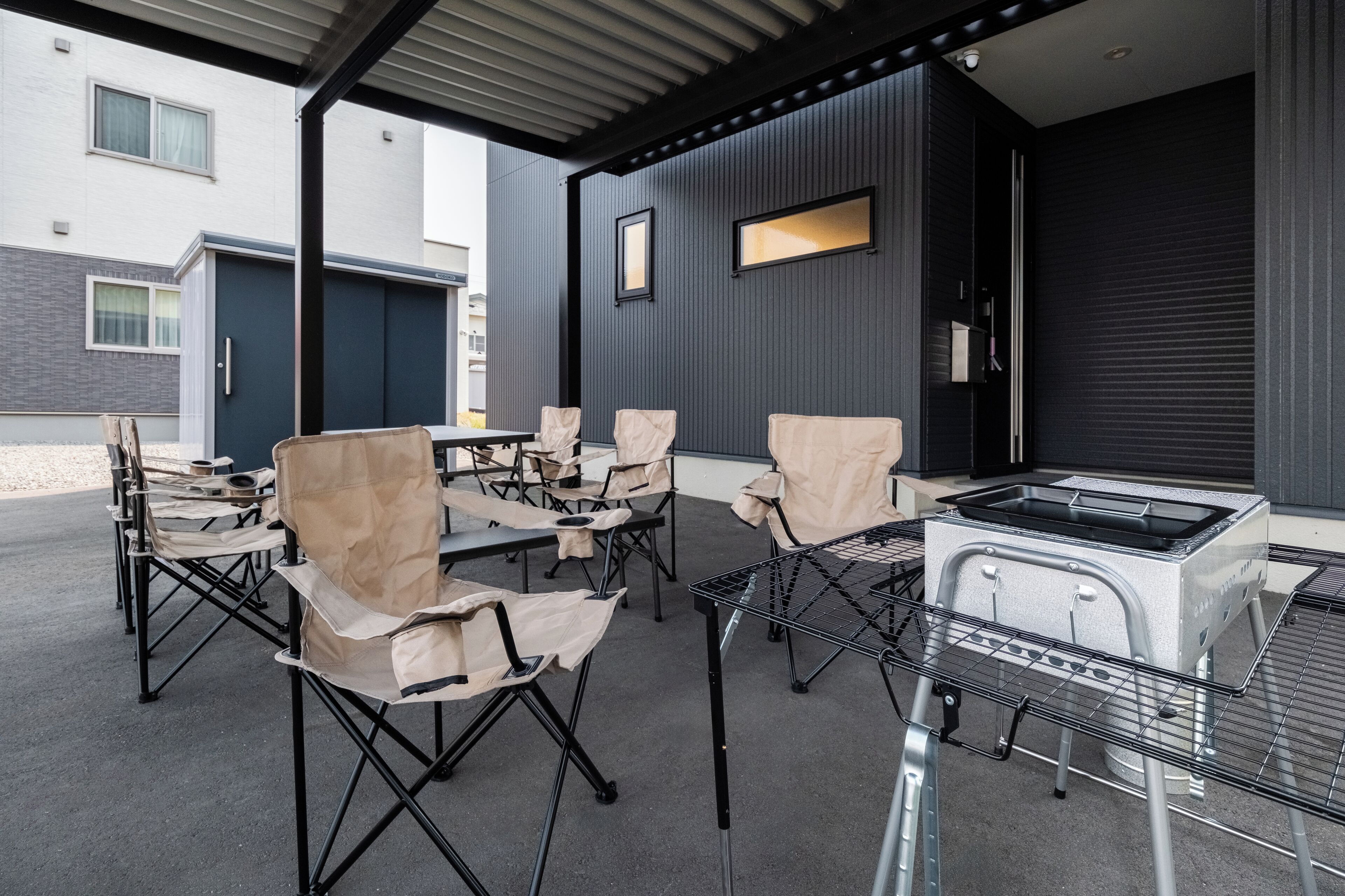 An outdoor patio area with a grill, foldable chairs, and a table.