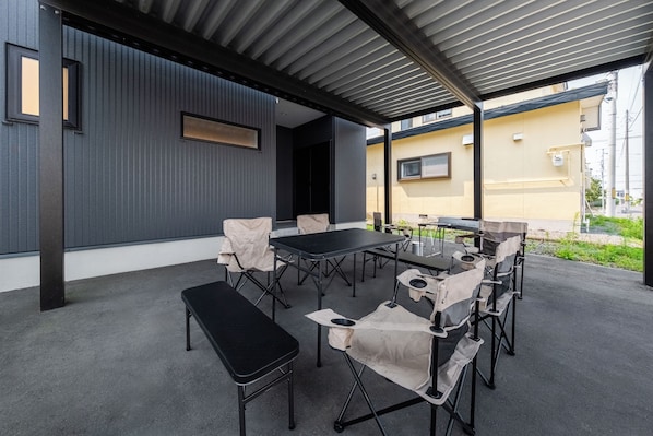 Un patio exterior con mesa y sillas, un banco y una zona cubierta con techo metálico.