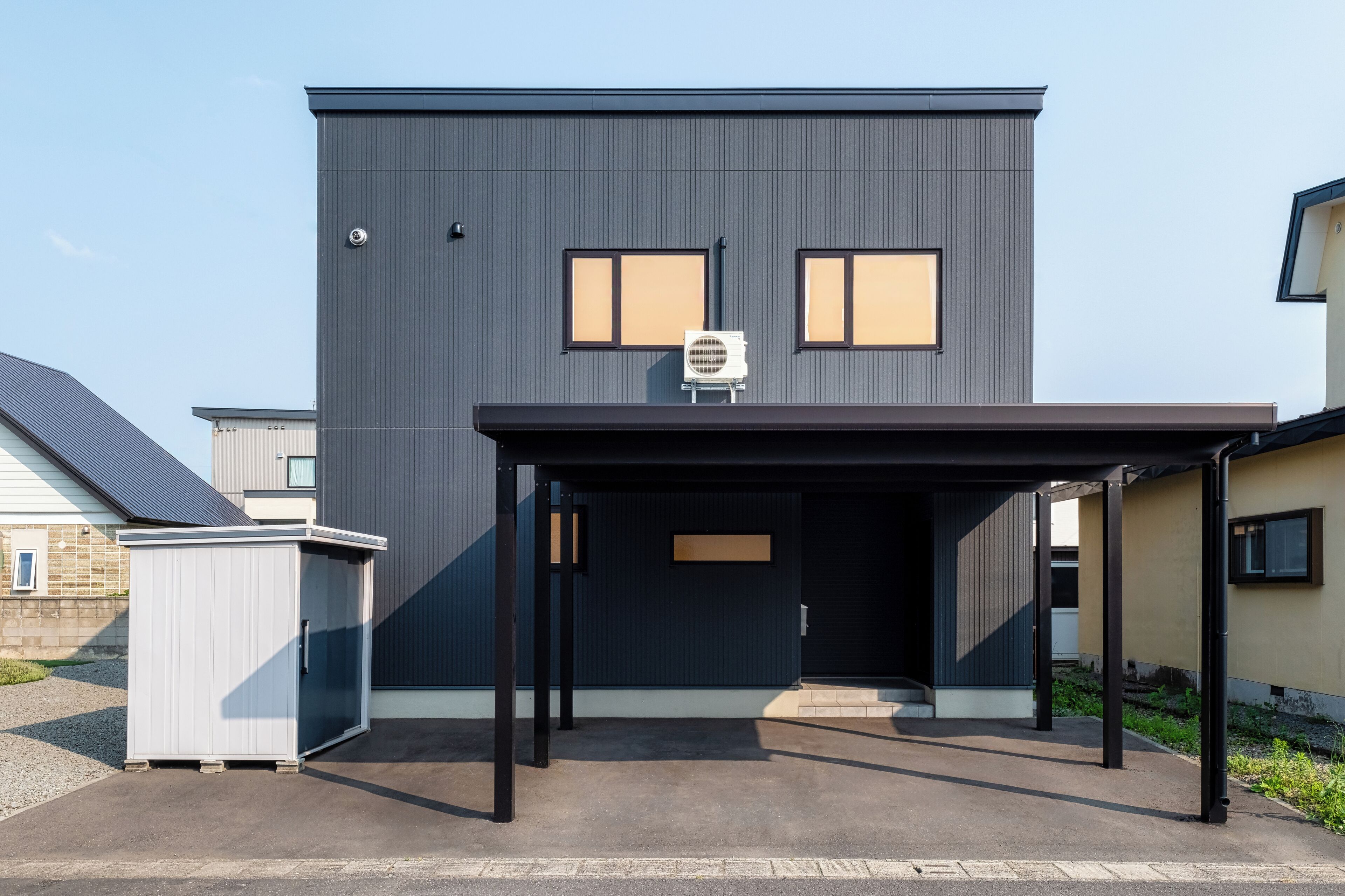 Een modern, twee verdiepingen tellend gebouw met een donkere gevel, twee ramen en een overdekte entree.