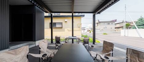 Un'area esterna coperta con tavoli e sedie, un ingresso protetto e vista sulla strada e sugli edifici sullo sfondo.