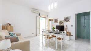 A modern living room with a sofa, dining table, and chairs. There is a TV on a stand, a plant, and artwork on the walls. - 4146 Giò House by Barbarhouse (Gallipoli)