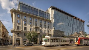 A modern building with a glass facade, a tram, and a red bus on the street. - Palazzo Vittoria Hotel Milano (Milan)