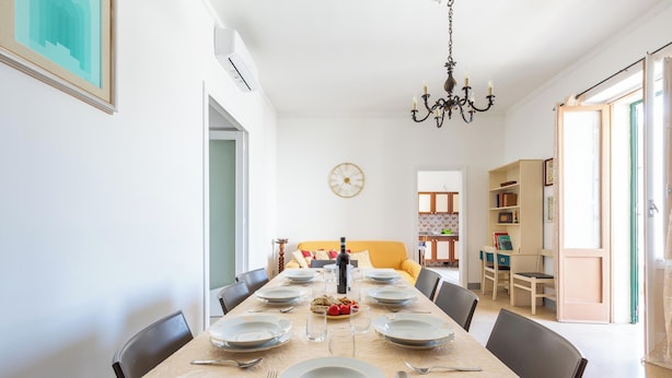 A dining area with a long table set for six, chairs around it, a chandelier, and a clock on the wall. - 4086 Maison Malù by Barbarhouse (Nardò)