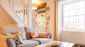 Una sala de estar acogedora con un sofá gris, almohadones coloridos, una mesa de centro de madera y un ventanal con vistas a la vegetación.
