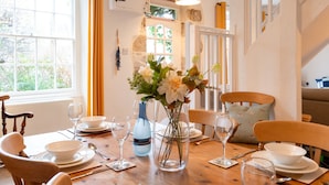 Comedor con una mesa de madera dispuesta para cuatro personas, rodeada de sillas. Un jarrón con flores se encuentra en el centro.