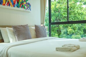 Une chambre d’hôtel avec une grande fenêtre, un lit recouvert de draps blancs et une peinture abstraite aux couleurs vives accrochée au mur.