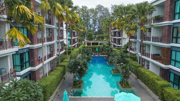 Ein Hotel mit einem zentral gelegenen Schwimmbecken, umgeben von üppiger Vegetation und Palmen.