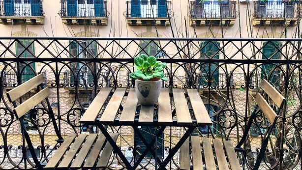 Un balcón con una mesa y sillas de madera, una planta en maceta y una barandilla de metal.