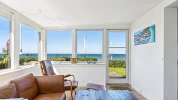 Une pièce avec un canapé en cuir, une table basse en bois et une vue sur la mer, grâce à de grandes fenêtres.