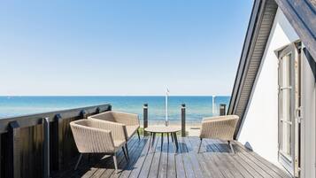 Une terrasse en bois, avec des chaises en osier et une petite table, donnant sur une mer calme.