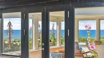 Une propriété située sur la côte, dotée de grandes fenêtres offrant une vue sur l’océan, d’un balcon avec des sièges et d’une vue sur la mer depuis l’intérieur.