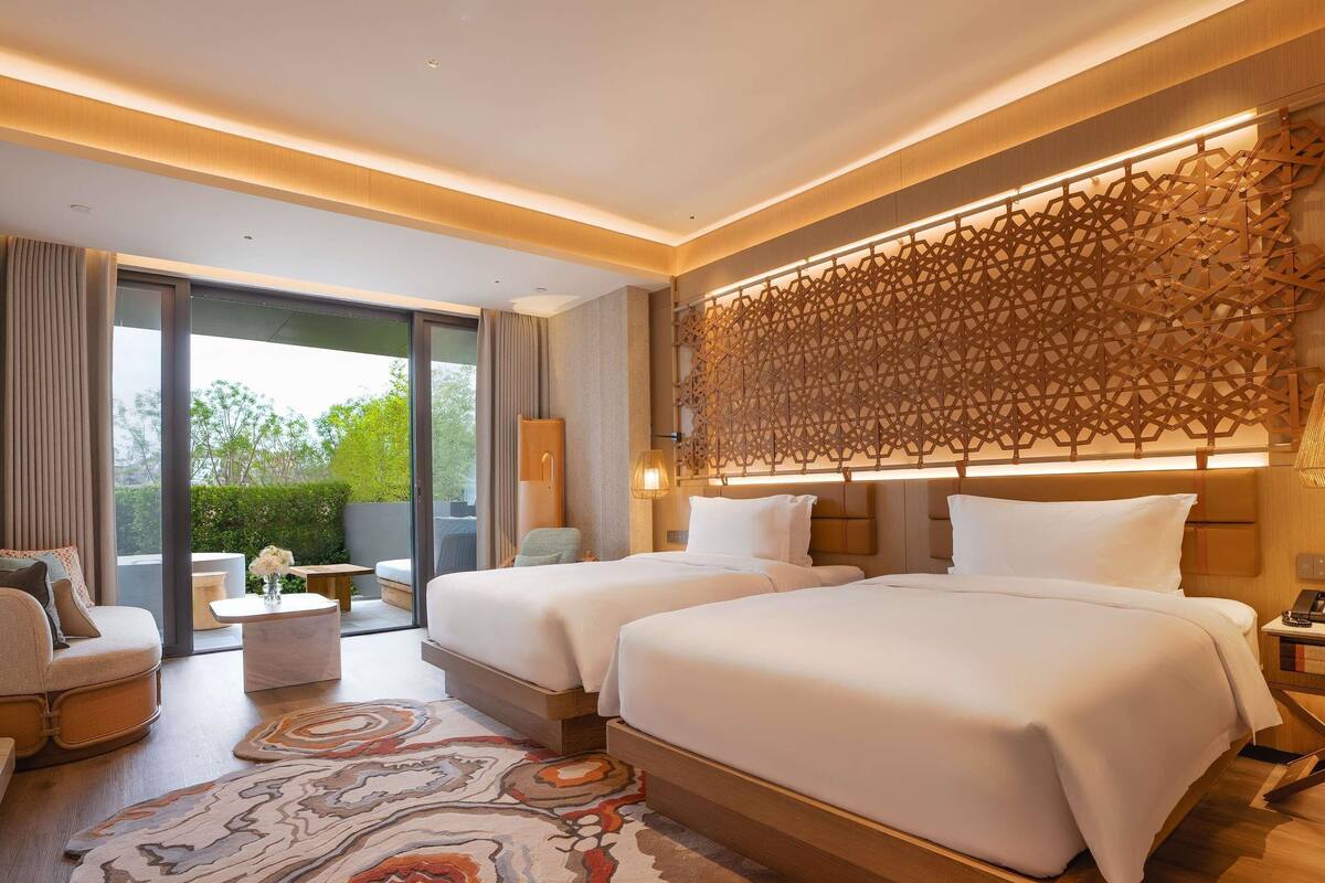 A modern hotel room with two beds, a large window, and a decorative wall panel.