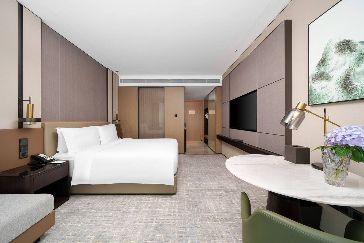 Une chambre d’hôtel avec un lit, une table de chevet, une lampe et une petite table sur laquelle se trouve un vase.