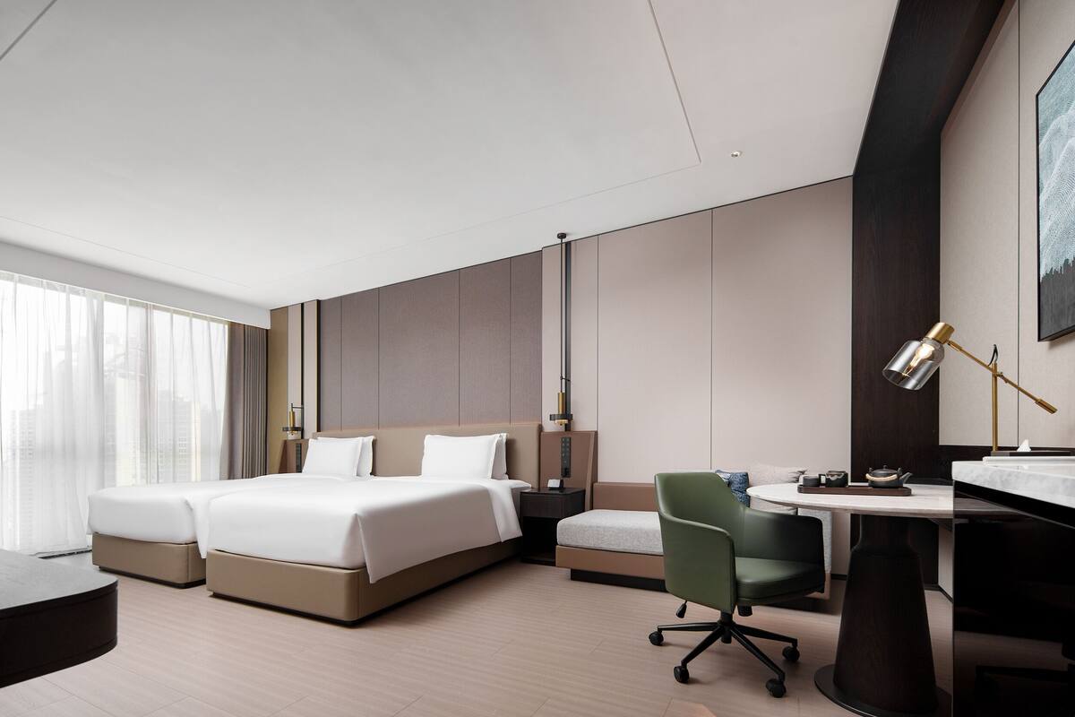 Une chambre d’hôtel moderne, dotée d’un grand lit, d’un bureau, d’une chaise et offrant une vue sur la ville.