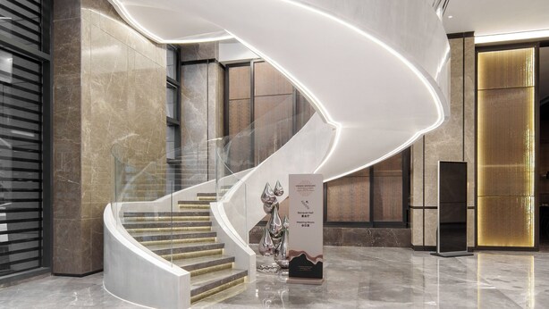 Un interior moderno con una escalera curva, pisos de mármol pulido y barandilla de vidrio.
