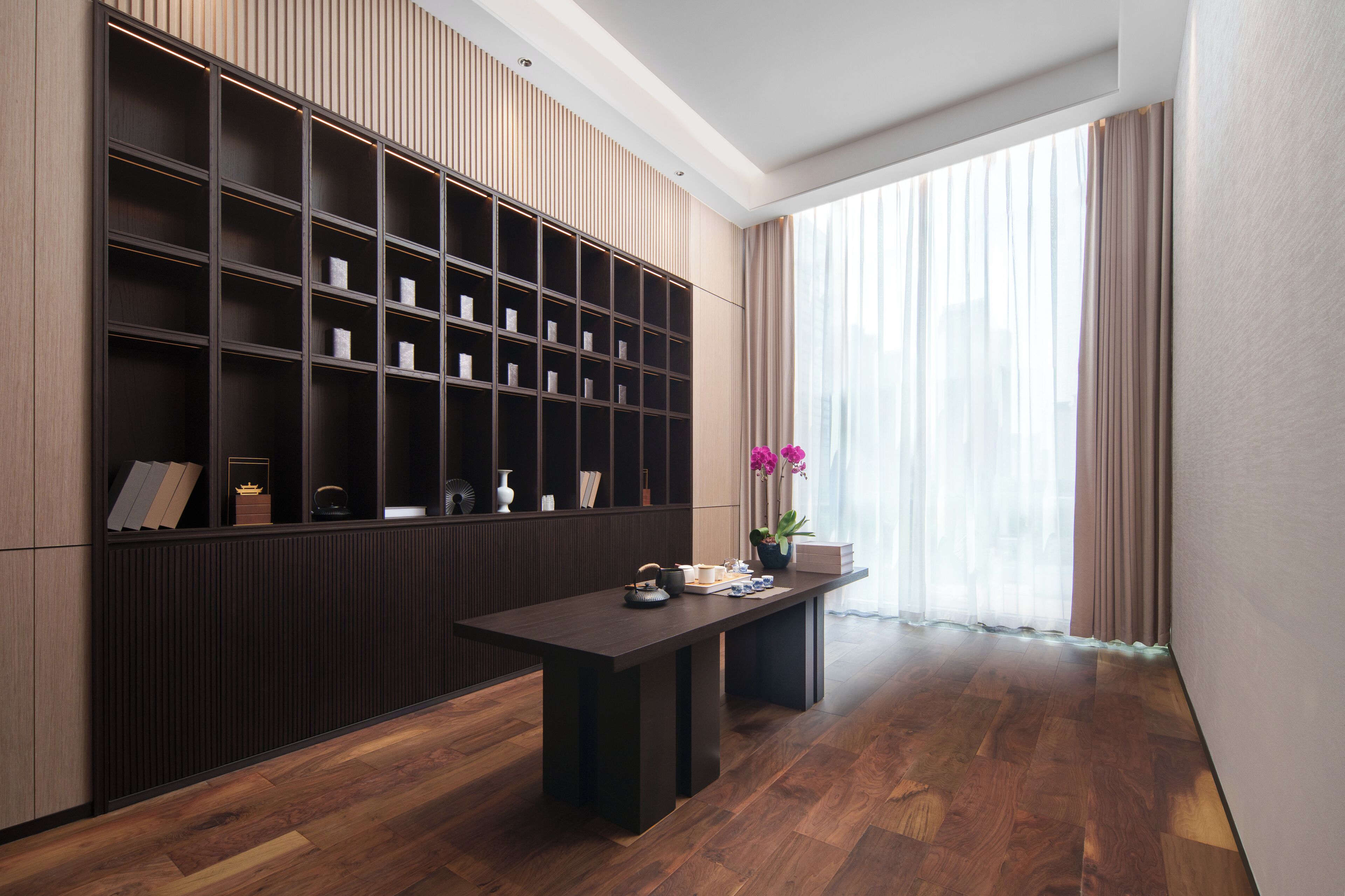 Una habitación moderna con piso de madera oscura, una amplia estantería y una mesa con un florero y una planta en maceta.