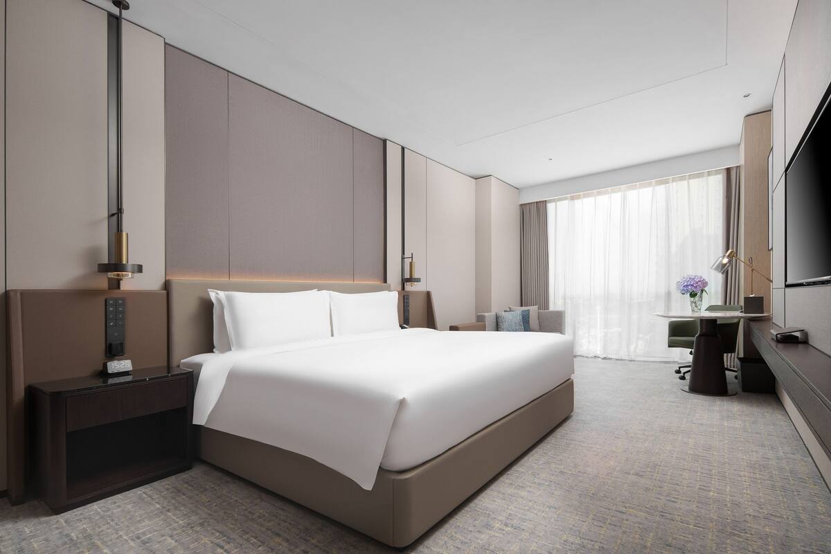 Une chambre d’hôtel moderne, dotée d’un grand lit, d’une table de chevet, d’une lampe et d’un téléviseur.