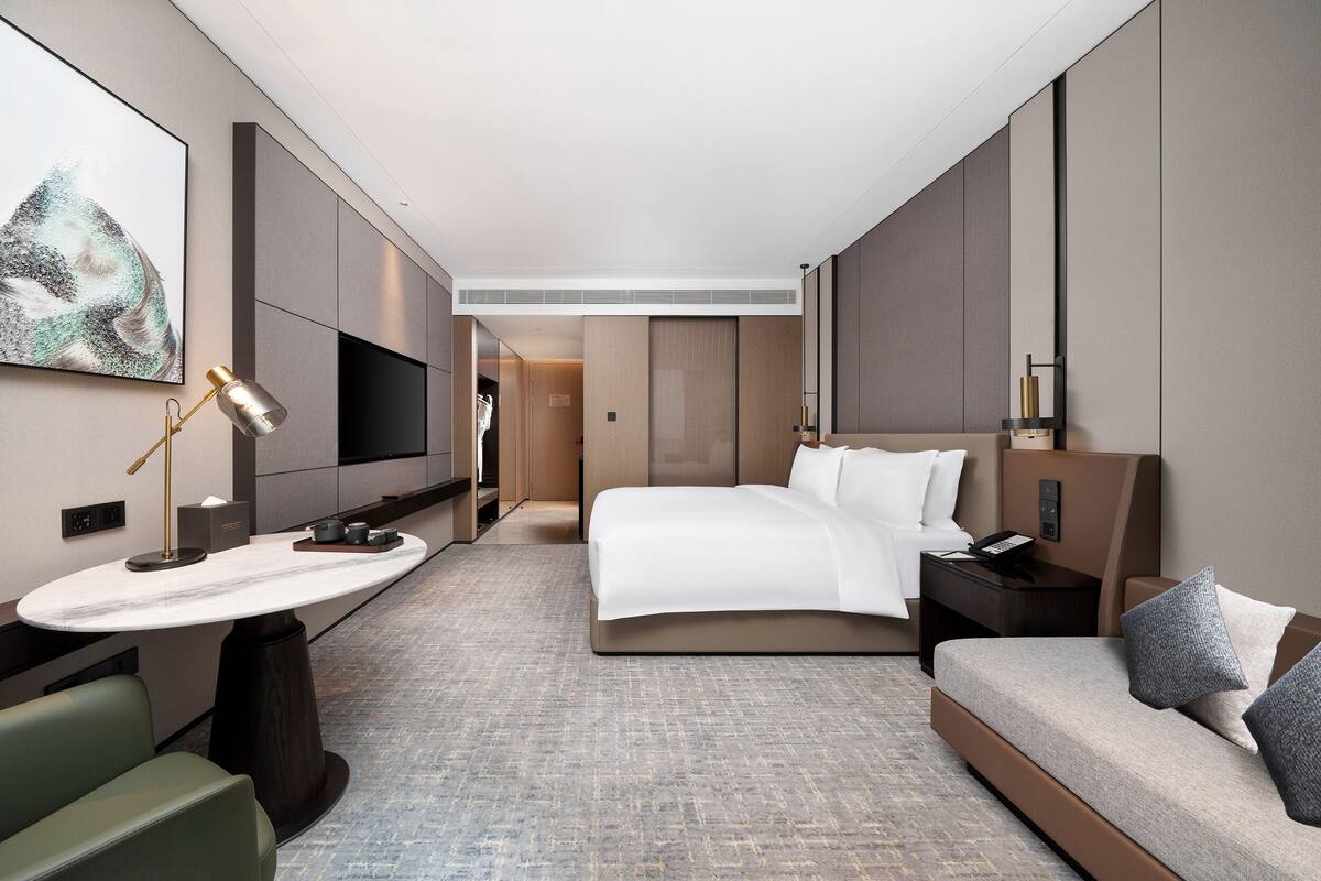 Une chambre d’hôtel moderne avec un grand lit, un bureau avec une lampe, une télévision et un canapé.