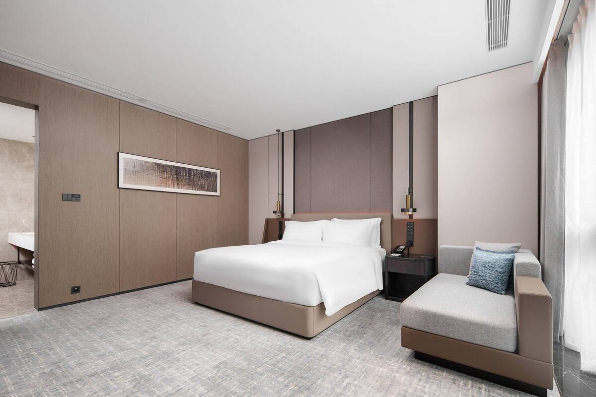 Une chambre d’hôtel moderne dotée d’un grand lit, d’un coin salon, d’une table de chevet et d’une œuvre d’art accrochée au mur.