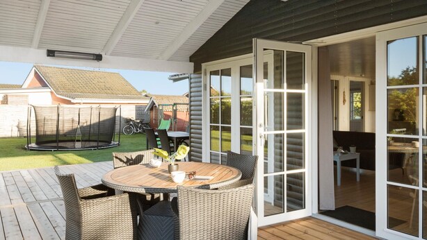 Eine Terrasse im Freien mit einem runden Tisch und Korbstühlen, einem Trampolin und einer Glastür zu einem Innenbereich.