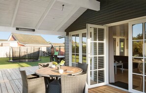 An outdoor patio with a round table and wicker chairs, a trampoline, and a sliding glass door leading to an indoor area. - Nice home in Hadsund with WiFi (Hadsund)