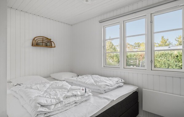 Um quarto branco com uma cama, uma janela e uma estante com plantas.