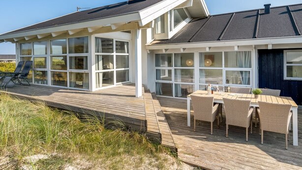 A modern house with a covered patio, large windows, and a wooden deck.