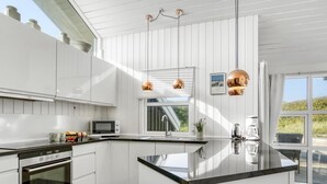 A modern kitchen with white cabinetry, a black countertop, and copper pendant lights.